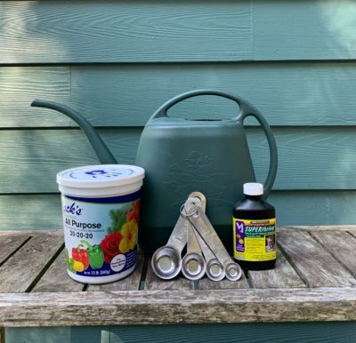 Watering can, fertilizer, and measuring spoons on gardening table.